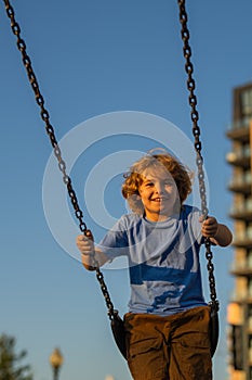 Kid swinging on chain swing on city kids playground. Swing ride. Cute child having fun on a swing on summer sky