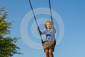 Kid swinging on chain swing on city kids playground. Swing ride. Cute child having fun on a swing on summer sky