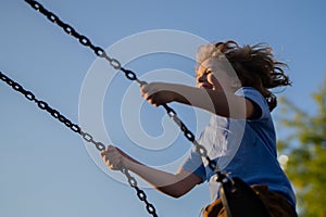 Kid swinging high. Adorable blonde child having fun on a swing on playground. Happy kid swinging on playground area