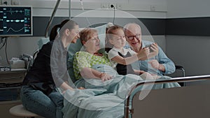 Kid taking selfie on smartphone with ill patient and family at visit