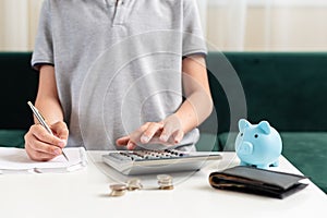 Kid teen boy counting money and taking notes, saving money in a piggy bank. Learning financial responsibility and