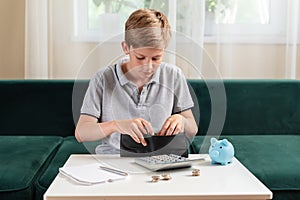 Kid teen boy counting money and taking notes, saving money in a piggy bank. Learning financial responsibility and