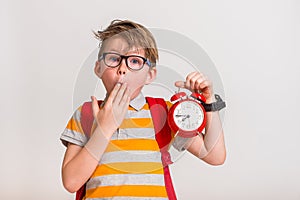 Kid and time. Child in glasses with backpack. Boy holding an antique clock over white background.