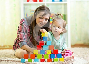 Kid toddler and mother build tower playing wooden toys at home or nursery