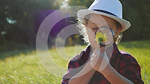 Kid tourist examines flower with a magnifying glass in the park. Travel tourism adventure concept. Little kid boyscout