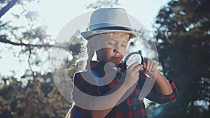 Kid tourist examines pine cone with a magnifying glass in park. Travel tourism adventure concept. Little kid boyscout