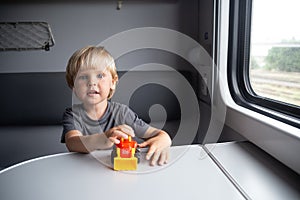 Kid in a train compartment looks out the window. The passenger with a toy travels in the train cabin