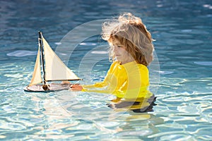 kid traveling on sea. Summer kids portrait. Little kid boy play with toy boat in the sea waves at the beach during