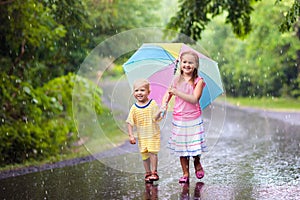 Kid with umbrella playing in summer rain.