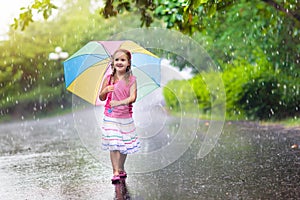 Kid with umbrella playing in summer rain.