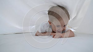 kid under the covers. baby boy crawling under the covers on the bed. happy childhood family playing at home concept