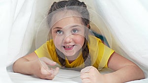 kid under the covers. baby girl crawling under the covers on the bed. happy childhood family playing at home concept