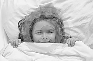 Kid under covers, face cover with blanket. Cute awaking child in bed, bedtime, childhood and growth kids concept, close photo