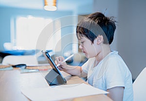 Kid using digital pen writing on tablet,Authentic Young boy using digital pad for his homework, Child studying online zoom video photo