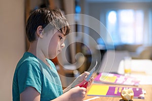 Kid using scissors cutting white paper ,Schoolboy making art and craft for his homework,Child learning how to use the scissors cut