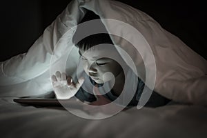 Kid using tablet while lying under blanket.