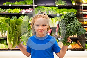 Kid with vegetables at grocery store. Healthy food for kids. Portrait of smiling little child with shopping bag at