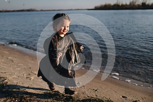 Kid walking on the beach in dark clothes. Warm autumn day. A lonely girl on the river Bank on sunset. Kids Emotions.