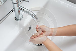 Kid washing hands in a white basin with a bar of white soap.