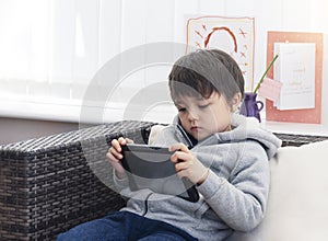 Kid watching cartoons on tablet, Little boy sititng on sofa with serious face playing games on smart phone,  indoors activities