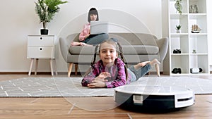 Kid watching robot vacuum cleaning when mom doing remote job
