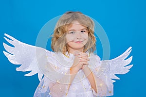 Kid wearing angel costume white dress and feather wings with prayer hands, hope and pray concept. Innocent child.