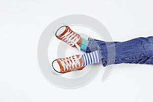 Kid wearing different pair of socks. Child foots in mismatched socks and red sneakers sitting on white background. Odd