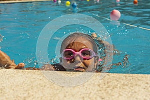 Kid wearing goggles breathing while swimming in the pool. Summer