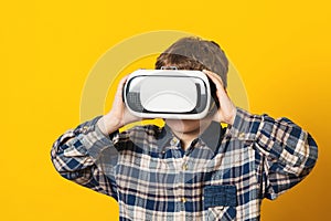 Kid wearing virtual reality glasses, isolated on yellow. Future technology. Boy using a virtual reality headset. Modern technology