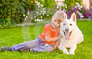 Kid and White Swiss Shepherd dog together on green grass