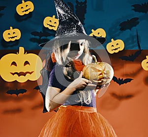 Kid in witch princess costume holds jack o lantern. Little witch wearing black hat. Halloween party concept