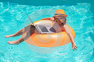 Kid working on laptop from the swimming pool. Work outside with laptop in pool.