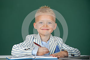 Kid writing in class. Child at school. Kid is learning in class on background of blackboard.