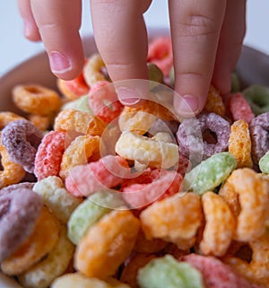 Kid's hand touching Colored Breakfast Cereal Close-up