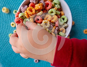 Kid's hand touching Colored Breakfast Cereal Close-up