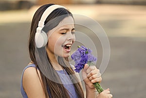 Kiddie song. Happy kid sing song outdoors. Using flowers as microphone. Little child enjoy singing in headphones