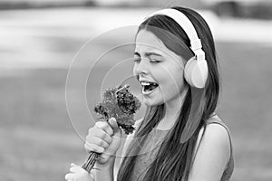 Kiddie song. Happy kid sing song outdoors. Using flowers as microphone. Little child enjoy singing in headphones