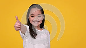 Kids approval. Studio portrait of cute positive little asian girl gesturing thumb up and sincerely smiling to camera