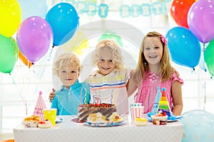 Kids birthday party. Child blowing out candles on colorful cake. Decorated home with rainbow flag banners, balloons. Farm animals