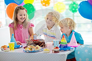 Kids birthday party. Child blowing out candles on colorful cake. Decorated home with rainbow flag banners, balloons. Farm animals