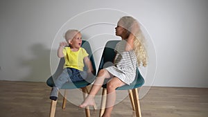 Kids boy and girl sitting on chairs and hitting each other with hands