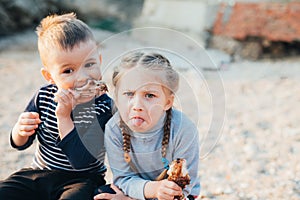 Kids brother and sister have fun eating chicken Shin on the beach near the sea and rocks