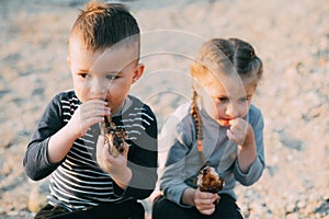 Kids brother and sister have fun eating chicken Shin on the beach near the sea and rocks