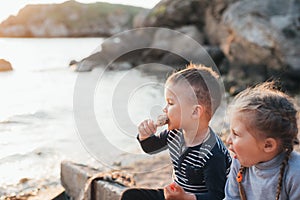 Kids brother and sister have fun eating chicken Shin on the beach near the sea and rocks