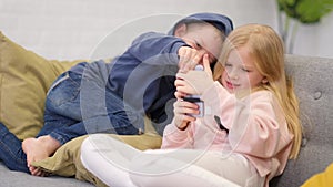 Kids brother and sister looking to smartphone screen at home. Little boy and girl playing online games on mobile phone.