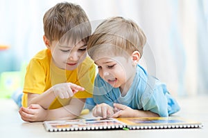 Kids brothers practice read together looking at book laying on the floor