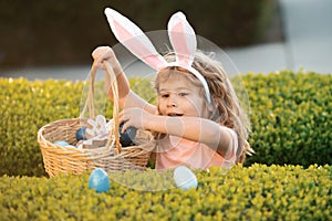 Kids in bunny ears on Easter egg hunt in garden. Child gathering eggs, easter egg hunt concept.