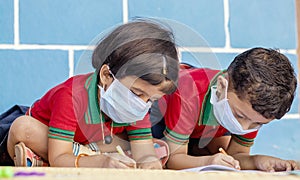Kids busy in writing with medical face mask wearing due to covid-19 or coronavirus outbreak or pandemic at school -
