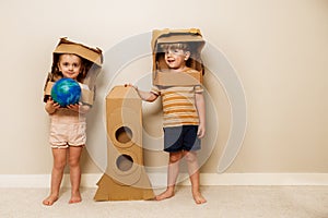 Kids with cardboard rocket and helmets hold model planet earth