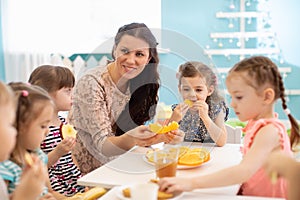 Kids and carer together eat fruit as a snack in the kindergarten, nursery or daycare